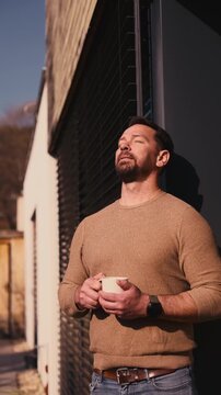 Relaxed man drinking coffee on terrace at home on sunny day.