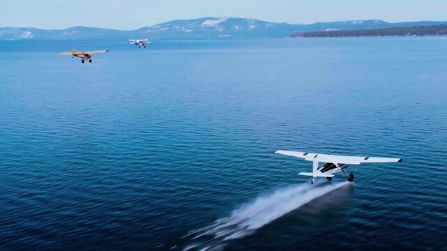 High angle drone perspective reveals floatplane touching down, generating spray, and skimming across alpine lake.