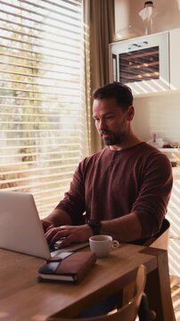 Man sitting in kitchen working remotely on laptop.