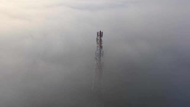 Communication tower emerging through thick fog with visible antenna and steel structure in a misty sky landscape illustrating technology and atmospheric conditions.