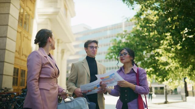 Three diverse business professionals engage in an animated discussion outdoors, reviewing important project documents and charts.