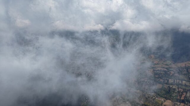 White clouds drift over rugged mountains. Valleys below hide in misty embrace at Wonokerto