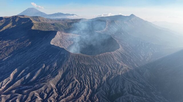 Aerial view of a smoking Mount Bromo volcanic crater. Rugged terrain surrounds the active vent