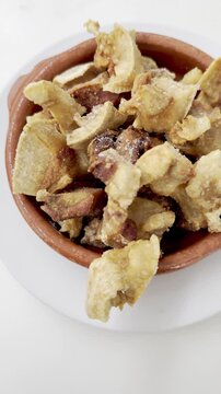 Close-up vertical panning footage showing detailed crispy Spanish morro de cerdo (fried pork snout) served as a traditional tapas dish in a small clay pot