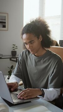 African American young adult man typing on laptop, thinking while studying. Ideal for remote work advertising, online education videos, tech promo, vertical