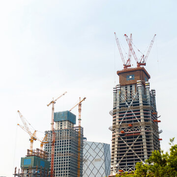 Modern skyscraper construction site with tall tower cranes building high-rise business towers against clear sky. Urban development, architectural engineering, and city growth concept.
