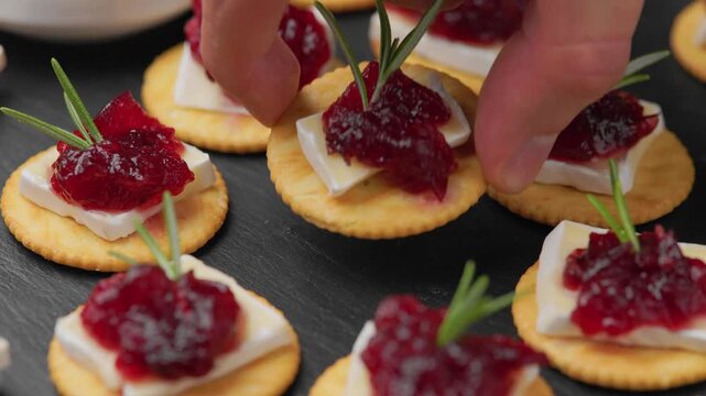 Hand picking up a cracker with brie cheese, cranberry sauce and fresh rosemary