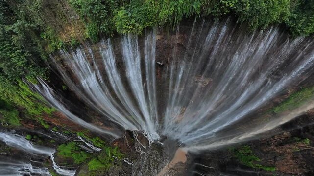 Dramatic fisheye aerial drone shot capturing radial cascades and lush cliffs at Tumpak Sewu waterfall.