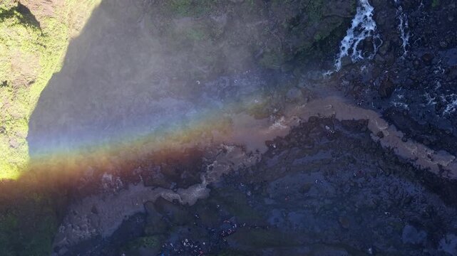 Aerial drone view of Tumpak Sewu waterfall with vivid rainbow reflection over rocky gorge.