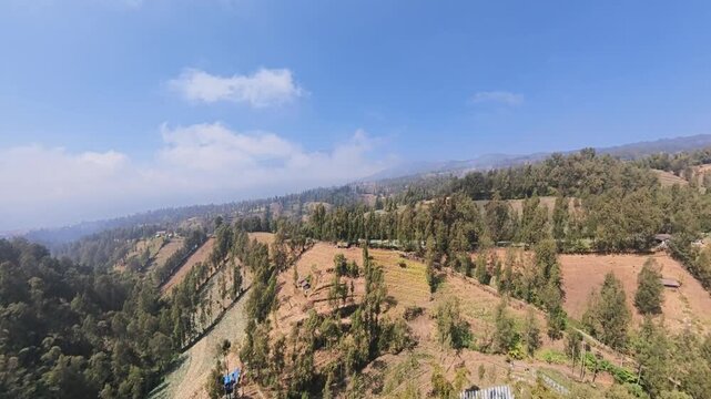 Wide aerial fisheye view of terraced hills, forests and clear blue sky at Cemoro Lawang.