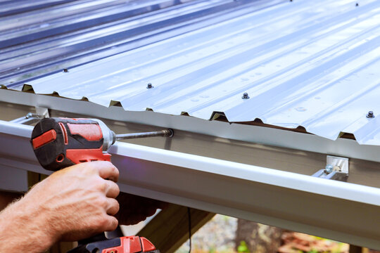 Worker is securing metal roof gutter panels on wooden frame in construction area outside.