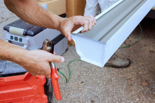 Worker is using tool to fasten metal gutter piece in workshop tools materials are nearby.