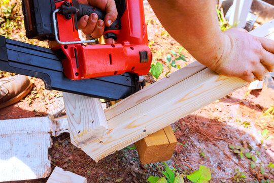 Worker man works with nail gun to join wooden boards together outdoors.