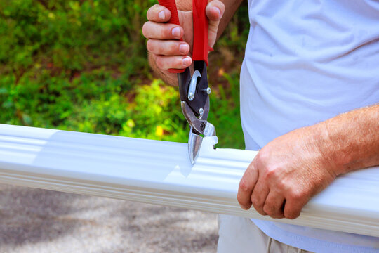 Contractor cuts edge gutter pipe trim in their backyard using pruning shears