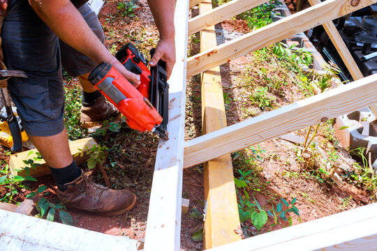 Construction worker is applying ail nail gun to connect two wooden beams on site
