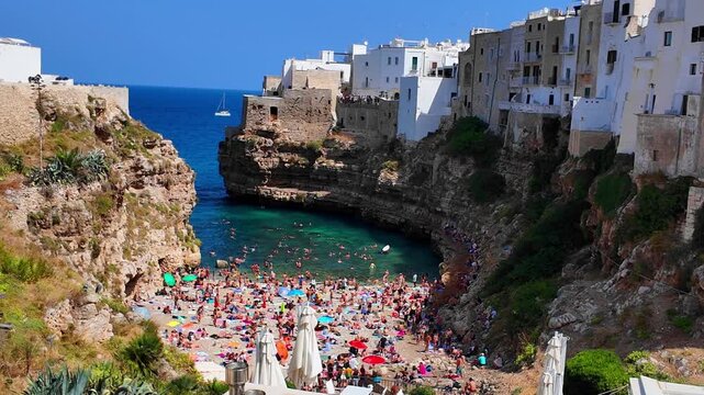 Scenic 4K stock footage of the famous Lama Monachile beach (Cala Porto) and the historic whitewashed cliffside old town of Polignano a Mare in Puglia, Southern Italy. Crystal-clear turquoise Adriatic 