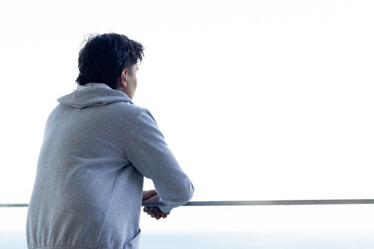 African American man leaning on balcony railing, holding phone, wearing gray hoodie, copy space