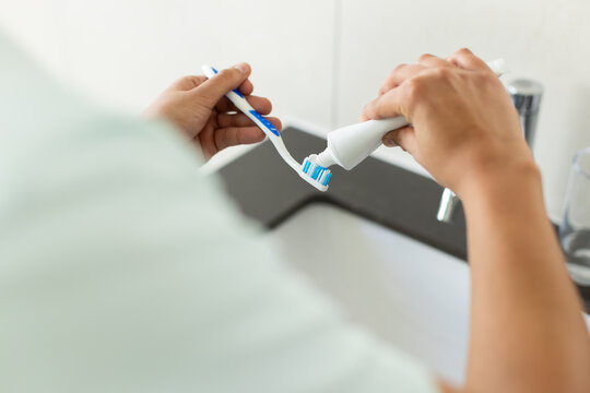 African American man preparing toothbrush, squeezing paste at bathroom sink with glass tumbler