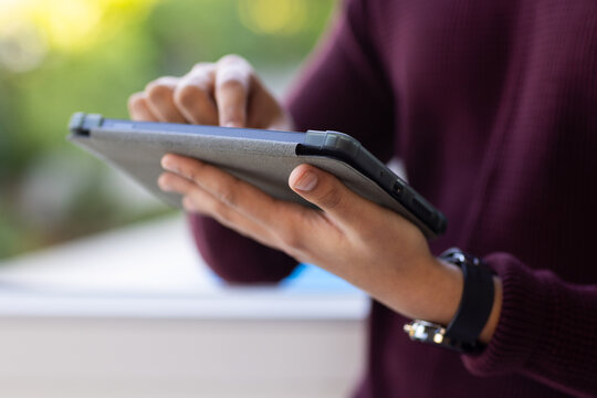 African American man holding tablet in folio, tapping screen on ledge, maroon sweater wrist strap