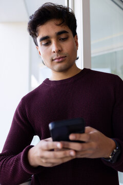 African American man in 20s holding phone, watch visible, wearing burgundy knit near glass wall