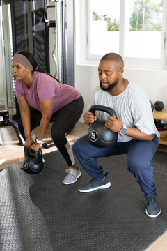African couple training in home gym on rubber mat, man holding 12 KG kettlebell, woman hinging