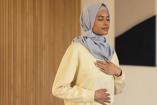 Woman in hijab, yellow sweatshirt standing and breathing at home near wooden slats, triangular art