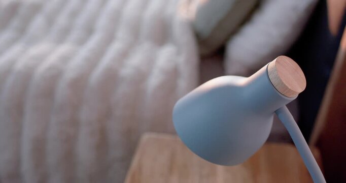Blue bedside lamp is tilting clockwise after touch, directing light down onto wooden nightstand