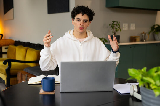African American man sitting, gesturing during virtual meeting at kitchen table with laptop and mug
