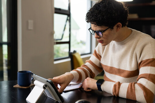 African American man in beige sweater with stripes sitting near open window using tablet on stand