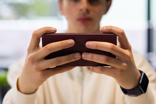 Man holding maroon smartphone in landscape at chest by window, in zip-up top and smartwatch