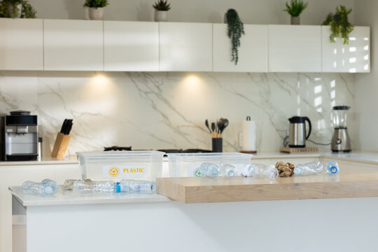 Clear plastic bottles are scattered on white kitchen island near recycling bins with PLASTIC label