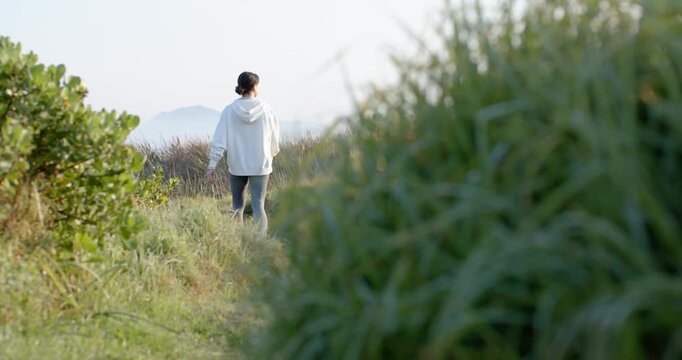 First step is starting woman walking along narrow coast path, emerging from tall grasses to hills