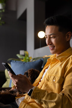 Mid-adult Asian man sitting on sofa, checking phone, wearing yellow shirt and smartwatch