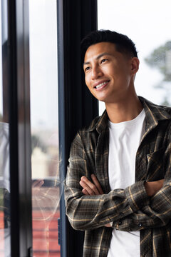 Asian man standing arms crossed inside by glass window plaid white tee reflection visible