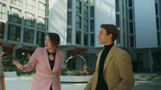 Professional business people meet and shake hands outside a modern office building. They engage in a friendly greeting and conversation in an urban setting.