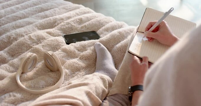 Wide start showing woman writing in lined notebook on plush blanket near window, journaling