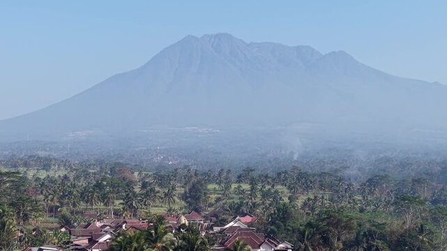 Misty mountain Kawi looms above verdant farmland. Rust colored roofs peek through tropical greenery