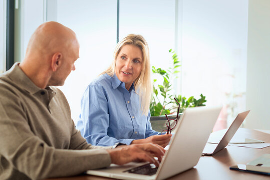 Mature businessman and female colleague collaborating on a laptop in a modern office conference room