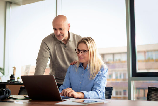 Mature businessman and female colleague collaborating on a laptop in a modern office conference room