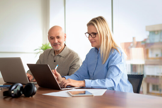 Mature businessman and female colleague collaborating on a laptop in a modern office conference room
