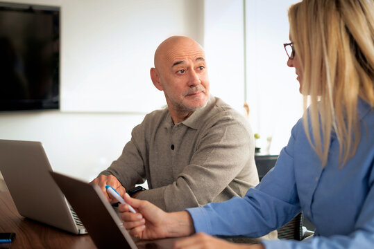 Mature businessman and female colleague collaborating on a laptop in a modern office conference room