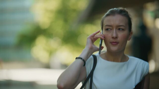 A young businesswoman walks outdoors while talking seriously on her smartphone. She is focused on her mobile conversation in an urban environment.