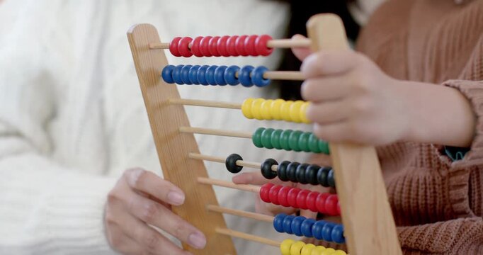 Diverse mother and son in sweaters counting on abacus at home, mother teaching son nudging beads