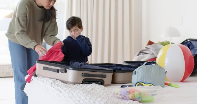 Asian mother and child packing suitcase, mother in green sweater picking red sweater for vacation