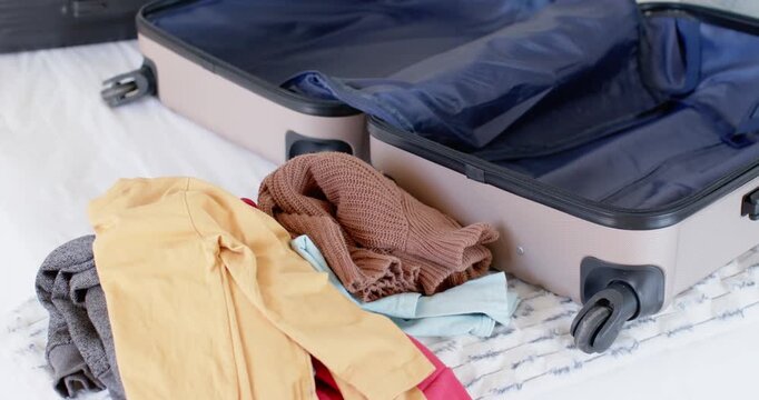 Camera is panning across bed, revealing open hard-shell suitcase and travel items, showing packing