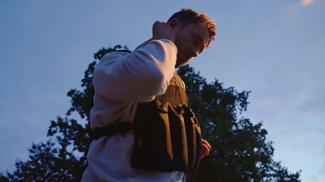 Young male athlete secures and tightens the straps of a black weighted vest before an outdoor evening run in slow motion.