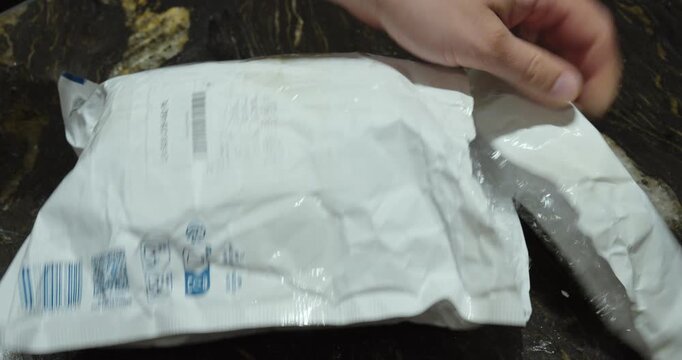Close up of hands tearing open a white padded shipping package and examining its protected contents on a dark countertop