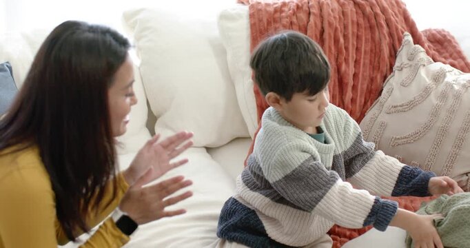 Mother and son on couch tapping urging folding blanket into basket, high-fiving and nose touching