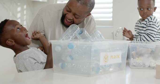 African American father and two sons leaning sorting PLASTIC bin at kitchen island teaching reuse
