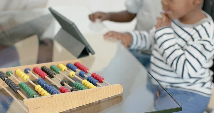 African American father leaning and pointing at tablet, guiding two boys from abacus toward table